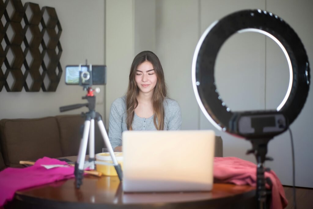 Home A young woman vlogging indoors using a smartphone, tripod, and ring light setup.